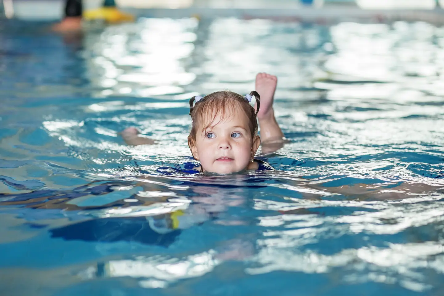 A preschool aged child swims alone in a pool with their head above water.